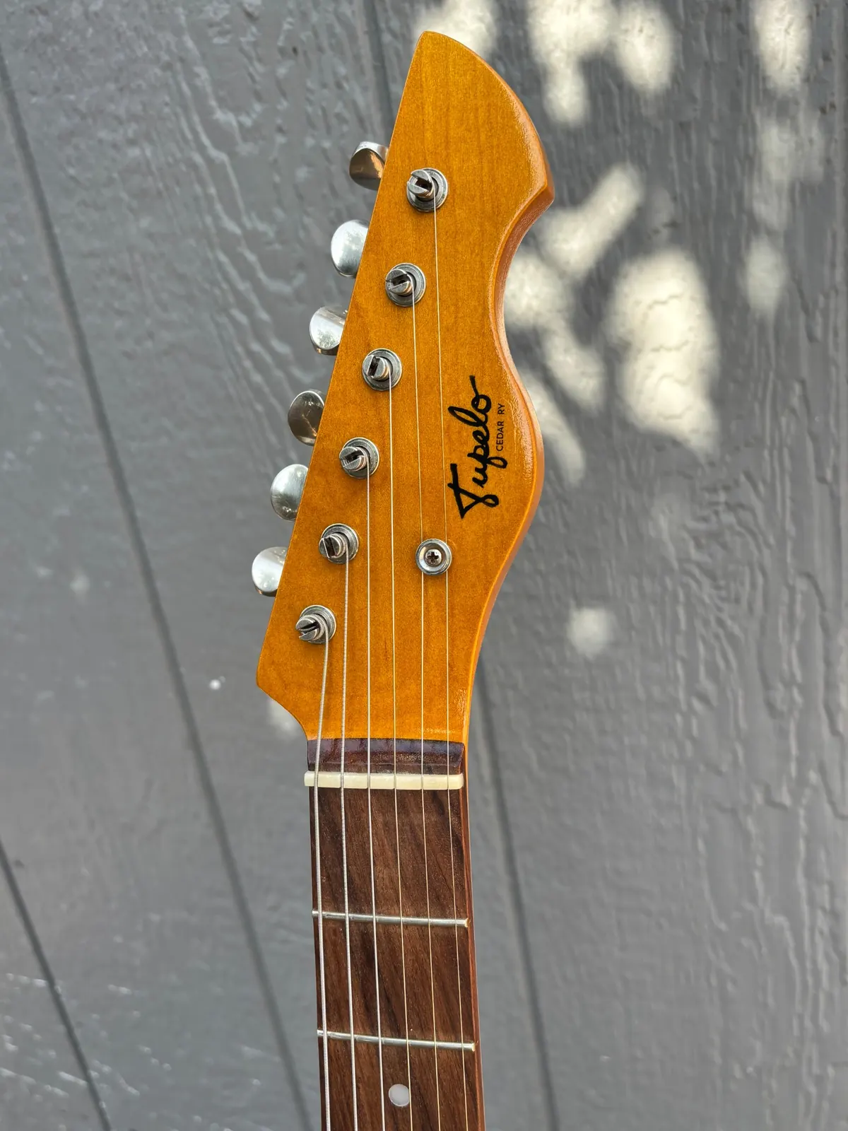 Plume headstock detail with Tupelo decal and six-inline tuners.